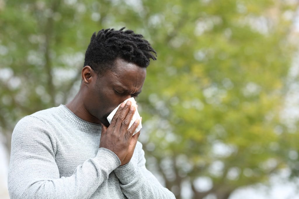 Allergic black man blowing on wipe in a park on spring season