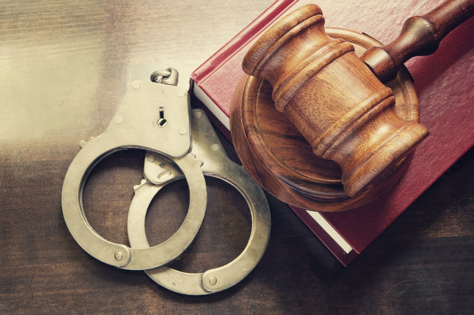 Gavel and handcuffs with red legal book on wooden table