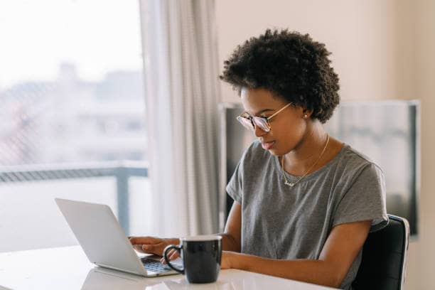 A young black beautiful woman is using a laptop in the living room at home.